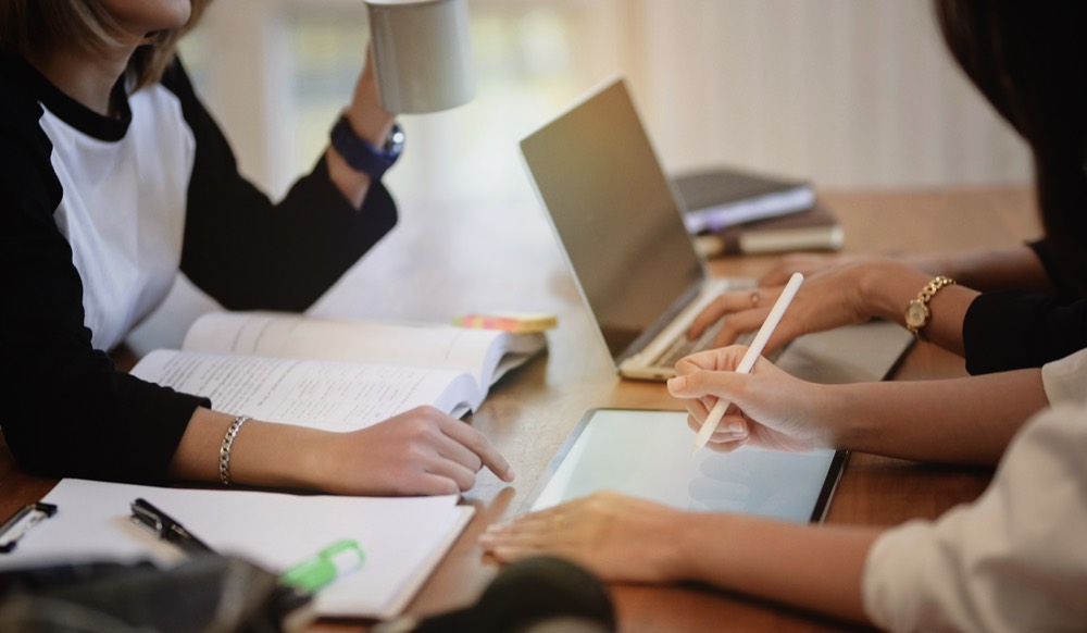 Students studying together at a table with a laptop, tablet, and textbooks